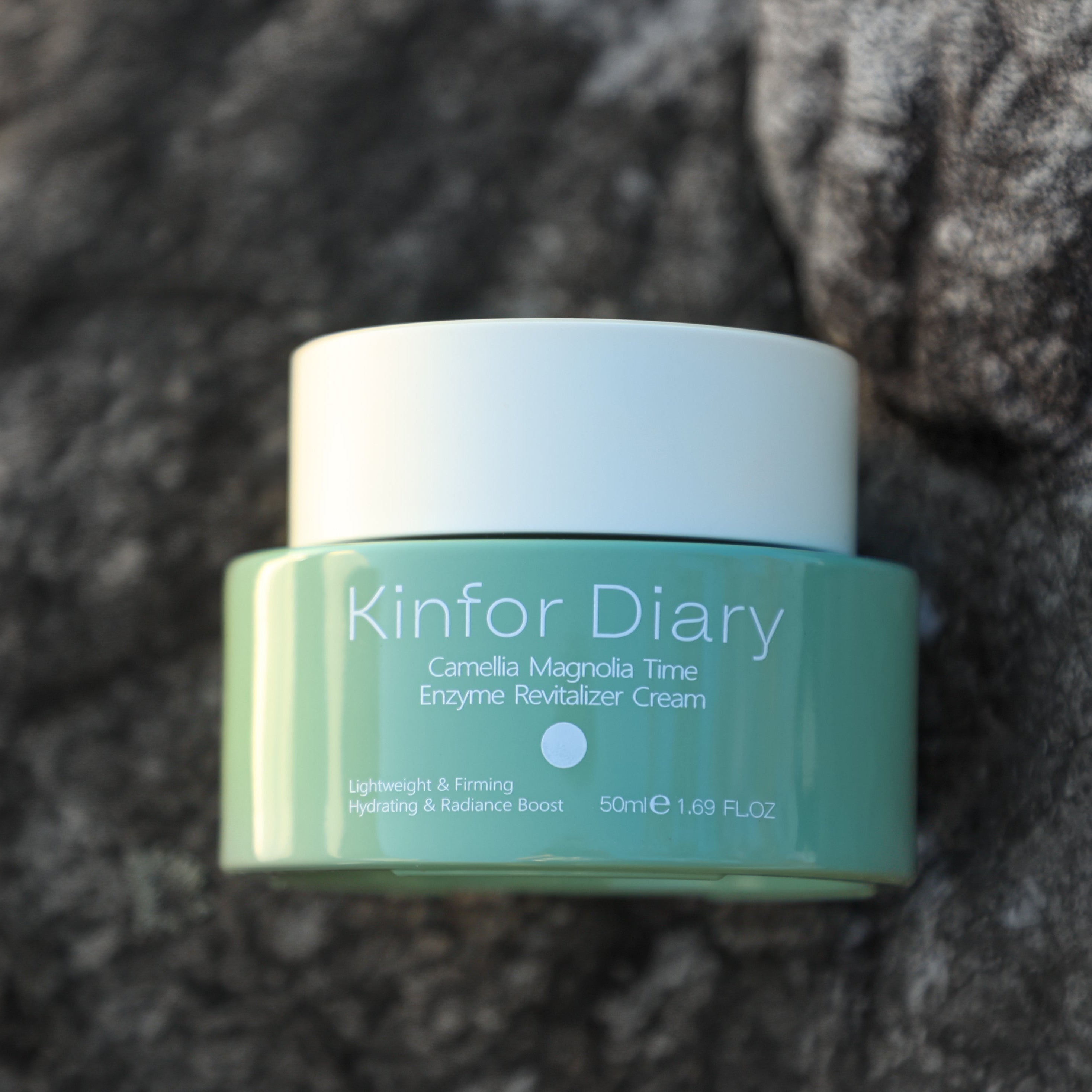 Green skincare product jar labeled 'Kinfor Diary' on a textured surface
